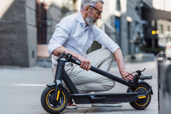Bearded and mature man adjusting electric scooter on street - foto de stock