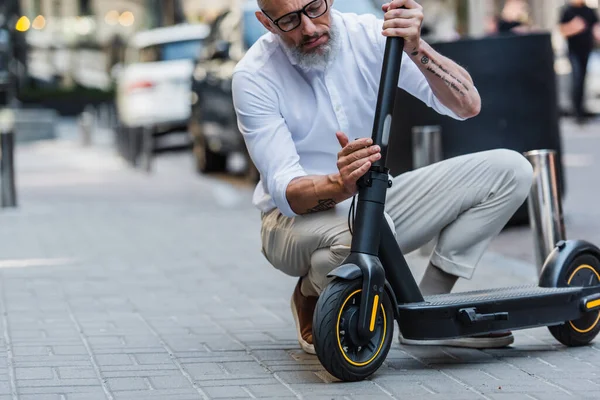Älterer Mann mit Brille und Hemd stellt Elektroroller auf der Straße ein — Stockfoto