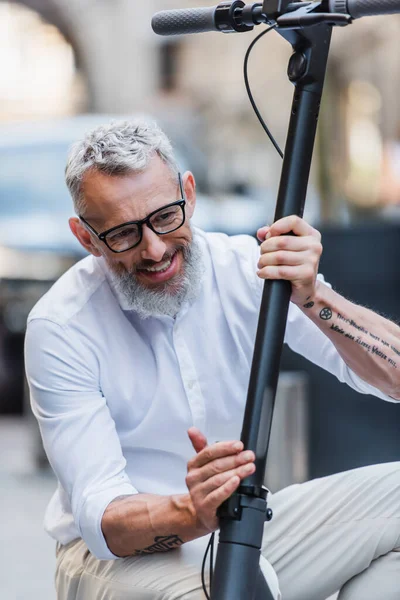 Positiver und reifer Mann mit Brille stellt Elektroroller auf der Straße ein — Stockfoto