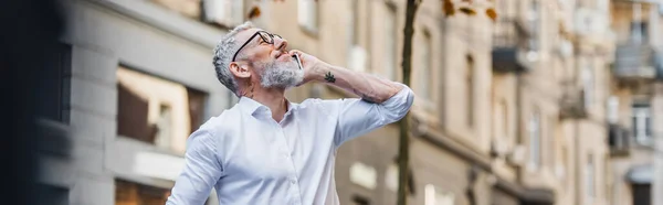 Glücklicher Mann mittleren Alters mit Brille, der auf dem Smartphone spricht und nach oben schaut, Banner — Stockfoto