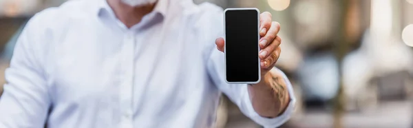 Обрезанный вид мужчины средних лет, держащего мобильный телефон с пустым экраном, баннер — стоковое фото