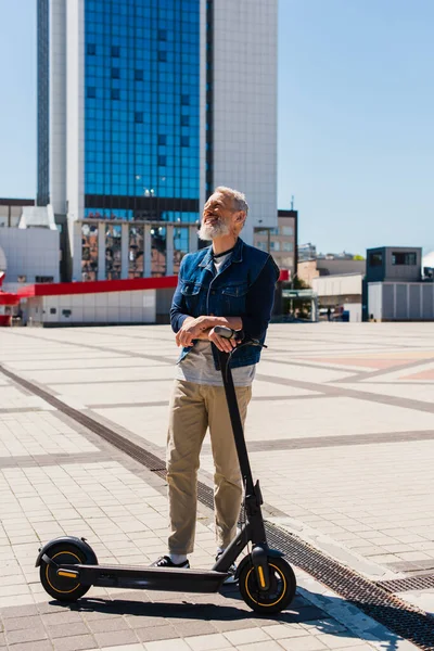 Voller Länge fröhlicher Mann steht neben E-Roller in der Stadt — Stockfoto