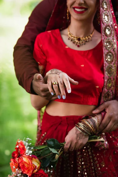 Vista cortada de homem indiano feliz segurando a mão da noiva com anel de casamento no dedo — Fotografia de Stock