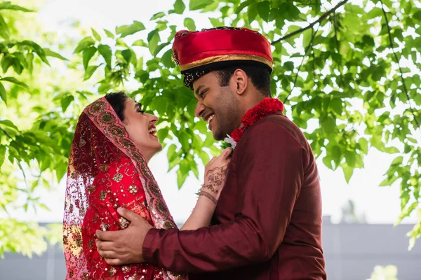 Side view of cheerful indian bride wearing garland on bridegroom — Stock Photo