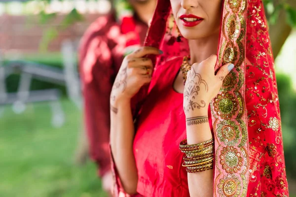 Vue recadrée de la mariée indienne en sari et foulard près de l'homme flou sur fond — Photo de stock