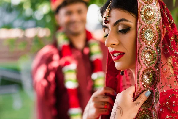 Индийская невеста в сари и платке возле размытого человека в тюрбане на заднем плане — стоковое фото