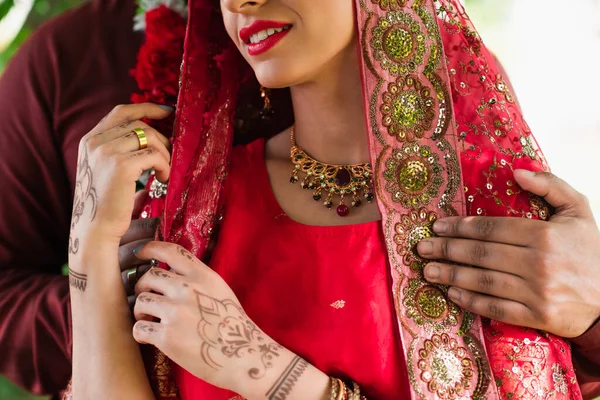 Recortado vista de indio hombre abrazando novia en rojo sari - foto de stock