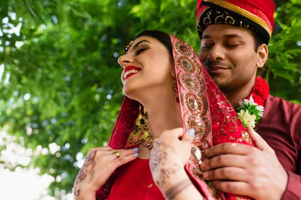 Vue à faible angle de l'homme indien heureux en turban étreignant mariée en sari rouge — Photo de stock