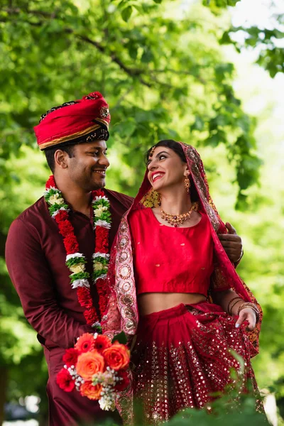 Hombre indio positivo en turbante abrazando novia en sari rojo - foto de stock