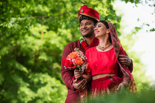Cheerful indian man in turban hugging bride in red sari — Stock Photo