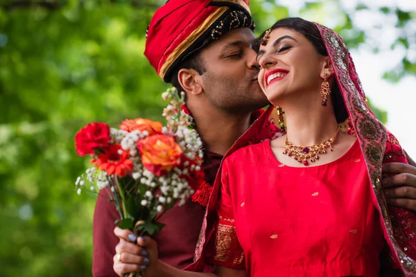 Indiana homem em turbante beijando feliz noiva em vermelho sari — Fotografia de Stock