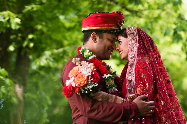 Вид сбоку, если счастливый индийский мужчина в тюрбане обнимает невесту в красном сари — стоковое фото