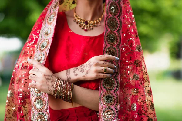 Partial view of young indian bride in red sari adjusting headscarf with ornament — Stock Photo