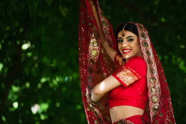 Счастливая индийская невеста в красном сари держит традиционный платок с орнаментом — стоковое фото