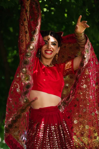 Happy indian bride in red sari and traditional headscarf with ornament posing outside — Stock Photo