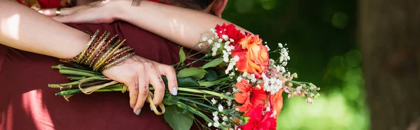 Vue recadrée de l'homme indien embrassant mariée avec des fleurs, bannière — Photo de stock