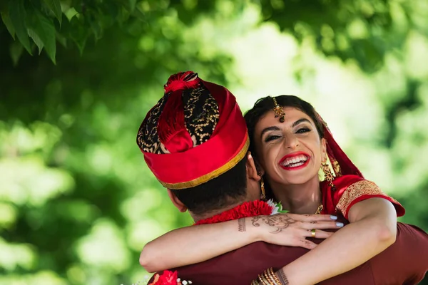 Rückseite des indischen Mannes im Turban umarmt glückliche Braut mit traditionellem Kopftuch — Stockfoto