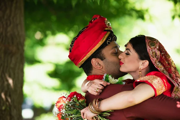 Indian man in turban kissing pretty bride in traditional headscarf — Stock Photo