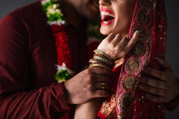 Partial view of blurred indian man in turban holding hand of happy bride in traditional headscarf isolated on grey — Stock Photo