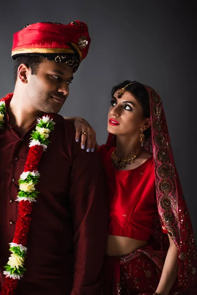 Hombre indio con turbante mirando a la novia bonita en el pañuelo tradicional aislado en gris - foto de stock