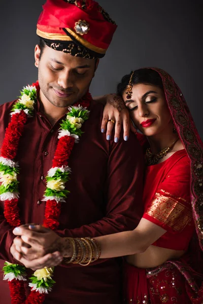 Indian man in turban holding hands with happy bride in traditional headscarf isolated on grey — Stock Photo