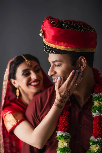 Размытое и веселое индийское невеселое прикосновение невесты к лицу жениха, изолированного на сером — стоковое фото