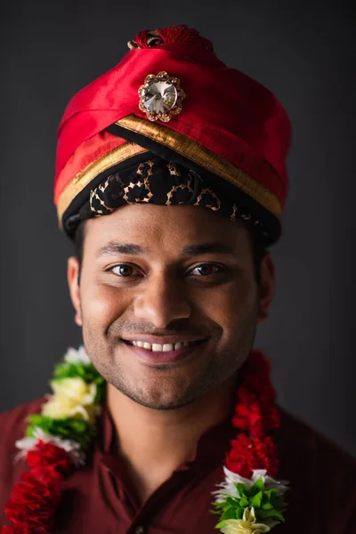 Positive indian man in turban and floral garland posing isolated on grey — Stock Photo