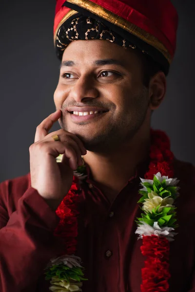 Hombre indio con turbante y guirnalda floral mirando hacia otro lado aislado en gris - foto de stock