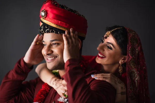 Cheerful indian bride hugging bridegroom in turban isolated on grey — Stock Photo