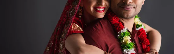 Vue recadrée de la mariée indienne gaie étreignant marié isolé sur gris, bannière — Photo de stock
