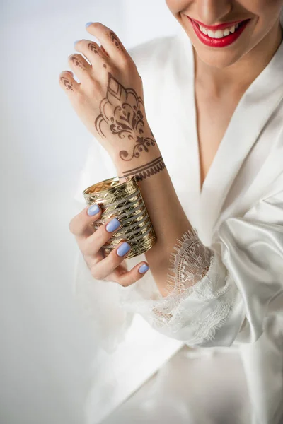 Vista recortada de la mujer india feliz con mehndi en la mano usando pulsera en gris - foto de stock