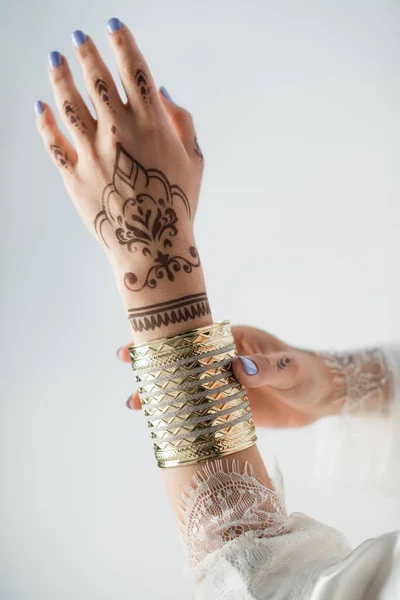 Vue recadrée de la femme indienne avec mehndi sur les mains portant bracelet en or tout en se préparant au mariage isolé sur blanc — Photo de stock