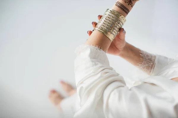 Vue partielle de la femme indienne avec mehndi sur les mains portant un bracelet en or tout en se préparant au mariage sur blanc — Photo de stock