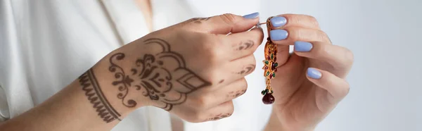 Cropped view of indian woman with mehndi holding earring isolated on white, banner — Stock Photo