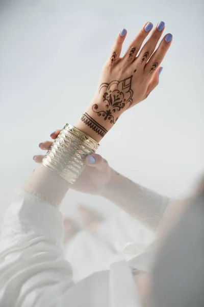 Vista parcial de la mujer india con mehndi usando pulsera de oro mientras se prepara para la boda en blanco - foto de stock