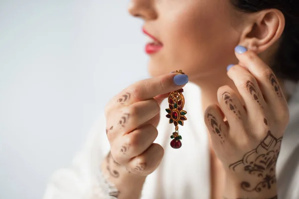 Vue recadrée de mariée indienne floue portant boucle d'oreille tout en se préparant pour le mariage isolé sur blanc — Photo de stock