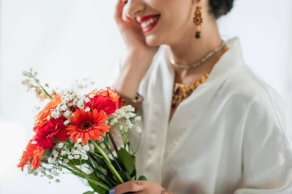 Vue recadrée de joyeuse mariée indienne tenant bouquet de fleurs sur blanc — Photo de stock