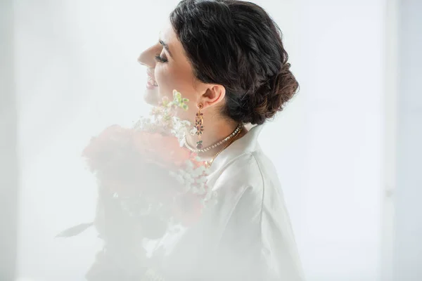 Vue latérale de heureuse mariée indienne avec mehndi tenant bouquet de fleurs sur blanc — Photo de stock