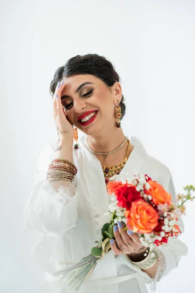 Cheerful indian bride with mehndi holding bouquet of flowers on white — Stock Photo