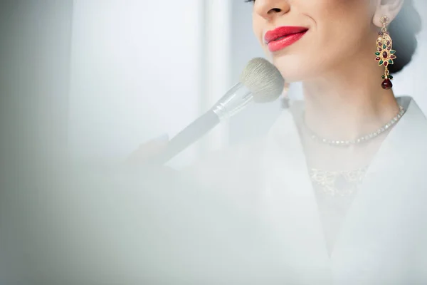 Vista ritagliata di donna indiana felice applicando polvere viso con pennello cosmetico su bianco — Foto stock