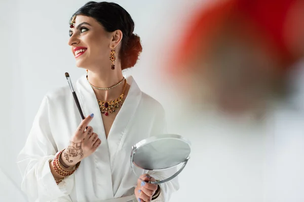 Noiva indiana alegre com mehndi segurando espelho e escova cosmética no branco — Fotografia de Stock