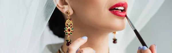 Cropped view of indian bride applying lipstick with cosmetic brush on white, banner — Stock Photo