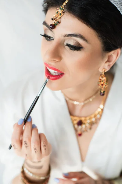 Indian bride applying lipstick with cosmetic brush on white — Stock Photo