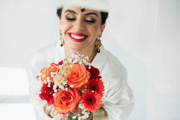 Jovem noiva indiana feliz com mehndi segurando buquê de flores no branco — Fotografia de Stock