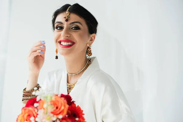 Молодая веселая индийская невеста с букетом цветов на белом — стоковое фото