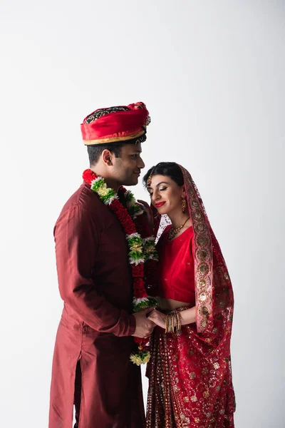 Счастливая индийская пара мужа и жены в традиционной одежде держась за руки изолированные на сером — стоковое фото