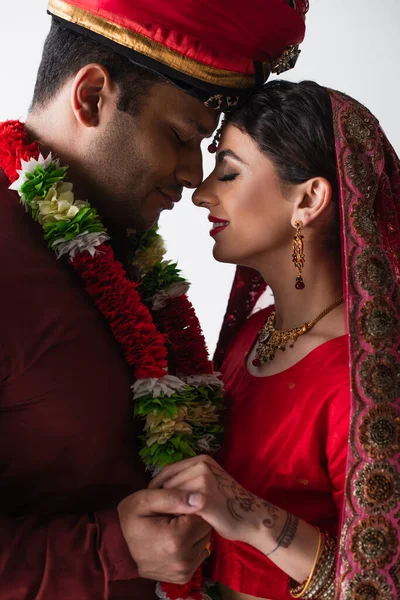 Seitenansicht eines lächelnden indischen Ehepaares in traditioneller Kleidung, das die Hände isoliert auf Weiß hält — Stockfoto