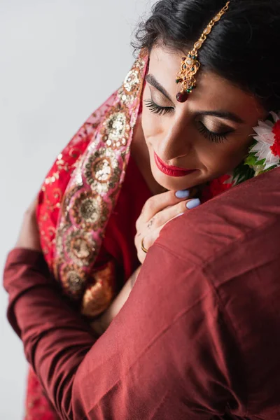 Жених обнимает индийскую невесту, изолированную от серых — стоковое фото