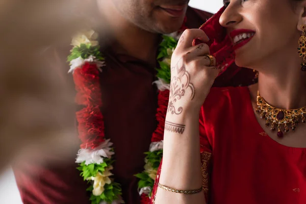 Vista recortada de la novia india alegre tocando el pañuelo de la cabeza y coqueteando con el novio - foto de stock