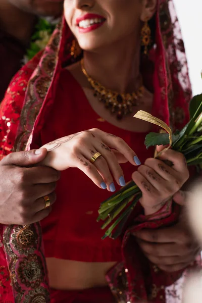 Частичный вид индийского мужчины, держащегося за руку счастливой невесты с кольцом на пальце, изолированном на белом — стоковое фото